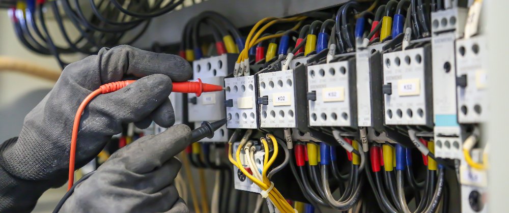 Electrical engineer using digital multi-meter measuring equipment to checking electric current voltage at circuit breaker in main power distribution board.